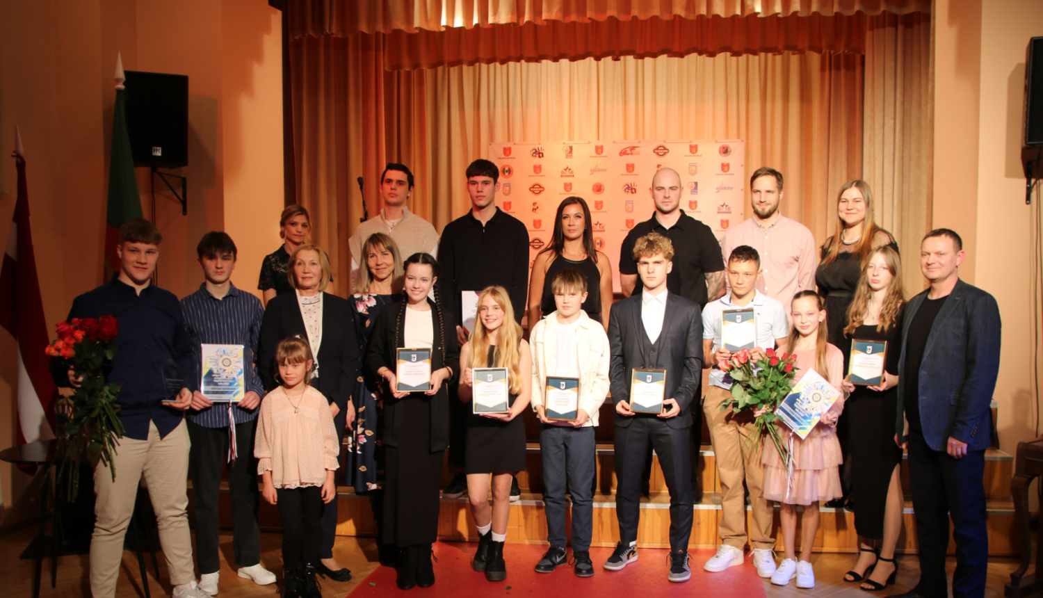 Kolektīva kopbilde ar skatuvi fonā