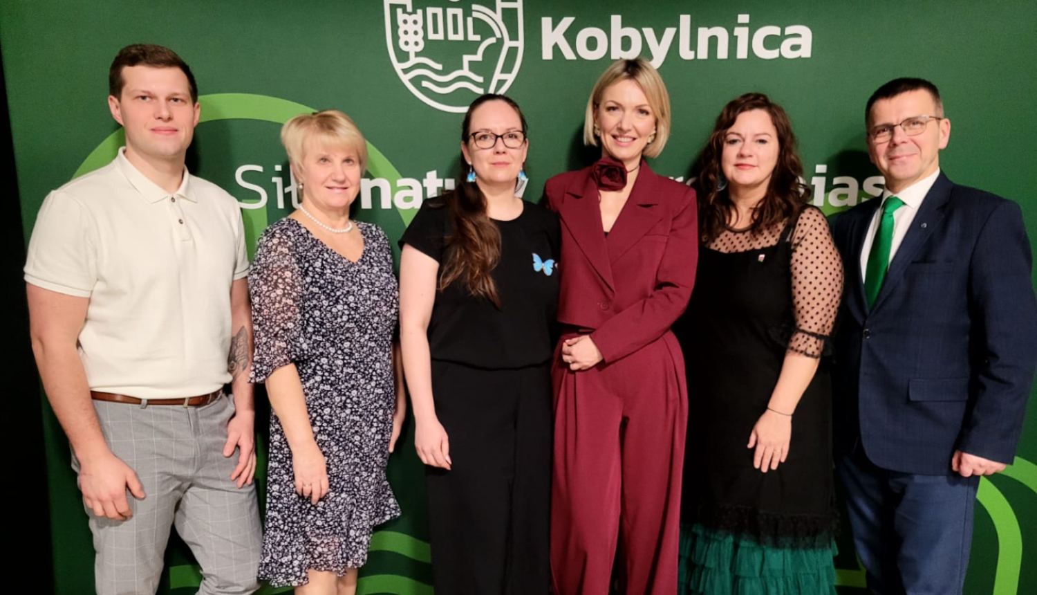 Sešu cilvēku kopbilde uz zaļa fona ar nosaukumu “Kobylinica”.