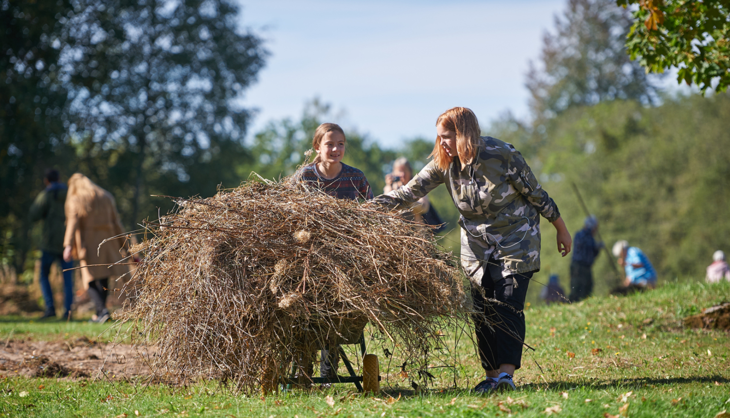 Divas jaunietes ar ķerru ved pērno zāli un zarus