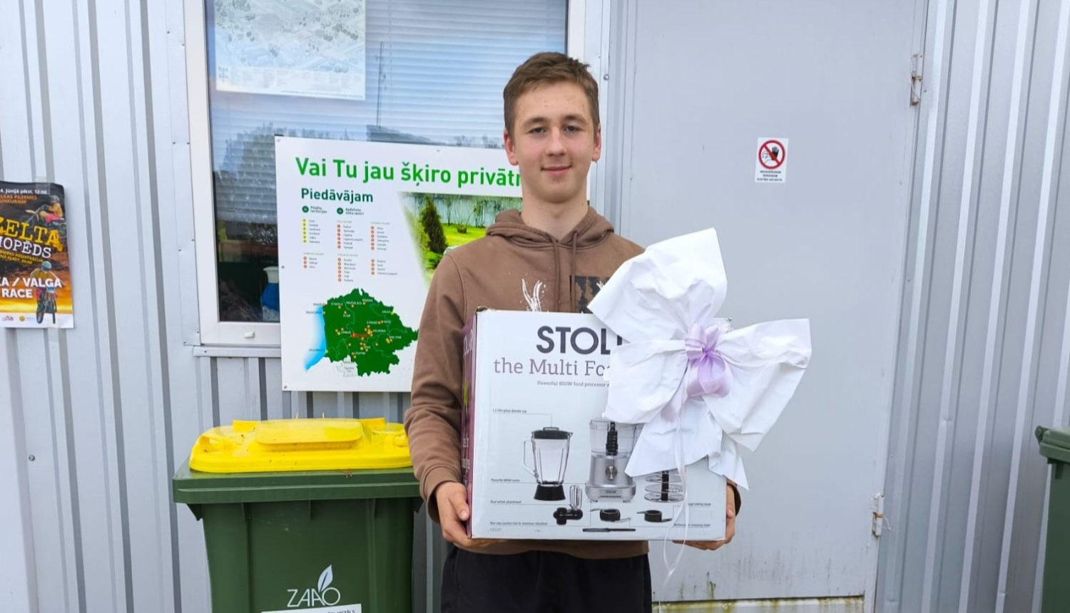 Smaidīgs jauns vīrietis, kurš rokās tur virtuves kombaina kasti