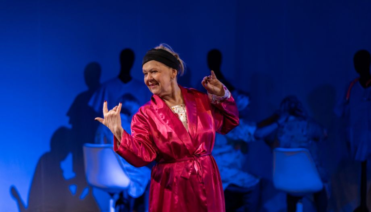 Aktieris sarkanā tērpā uz zila skatuves fona