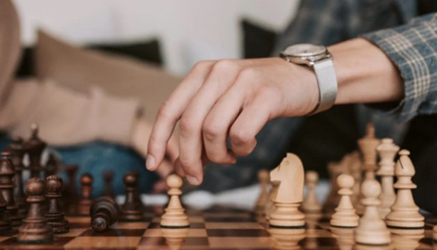 Cilvēka roka virs šaha galdiņa gatavojas veikt gājienu ar bandinieka kauiņu