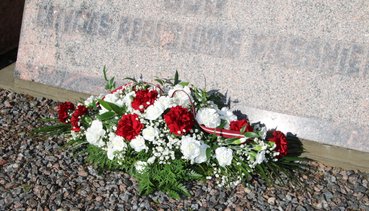 Sarkanu un baltu ziedu oāze pie piemiņas akmens