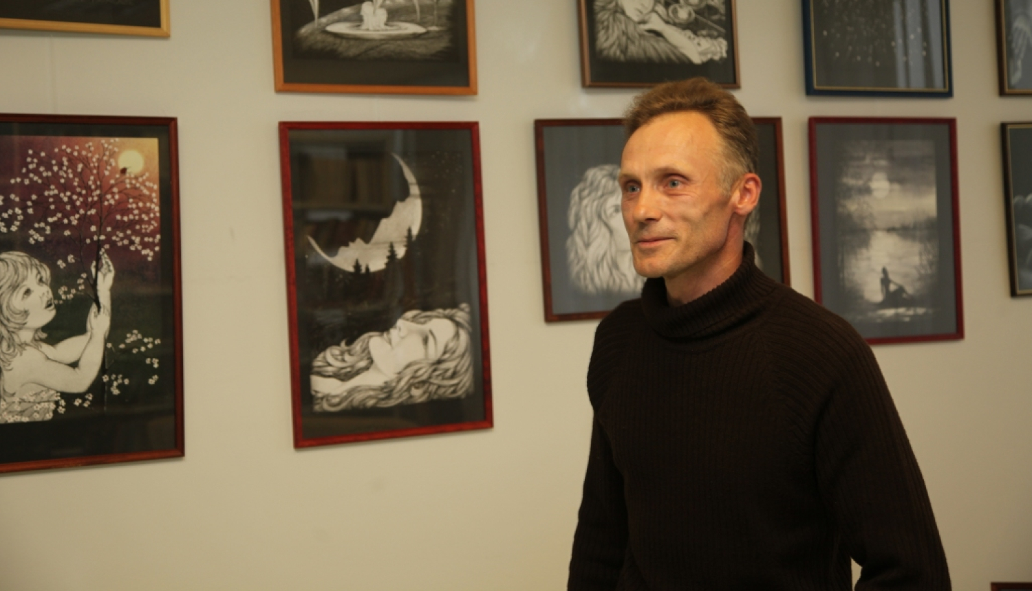 Vīrietis pusmūža vecumā pie sienas ar gleznām