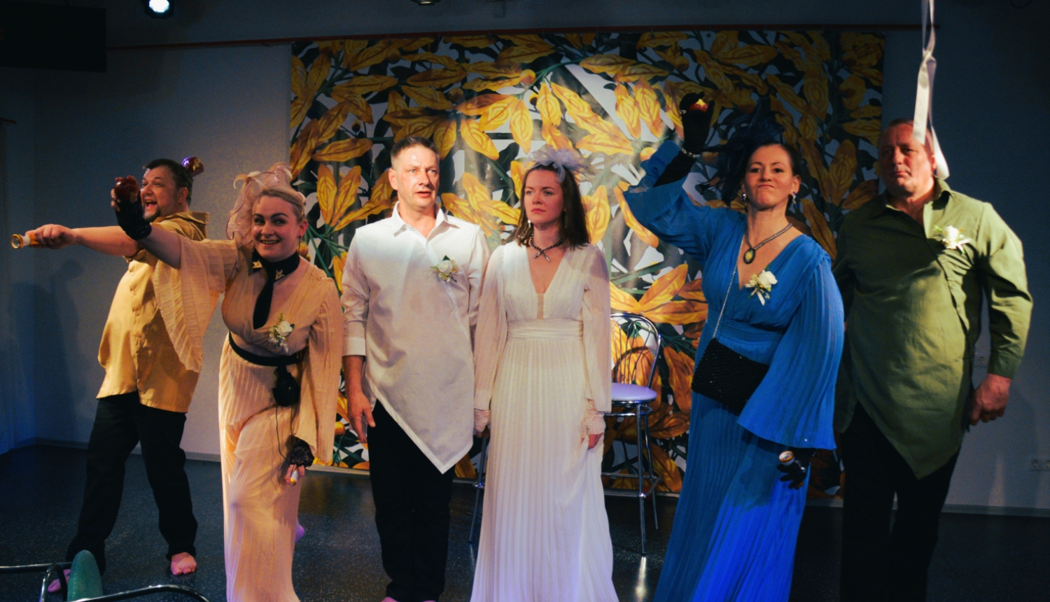 Seši cilvēki košos tērpos uz teātra skatuves