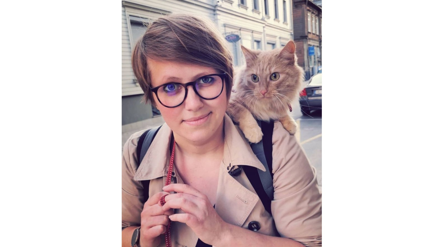 Sieviete ar īsiem, gaiši brūniem matiem. Viņai uz pleca ruds kaķis.
