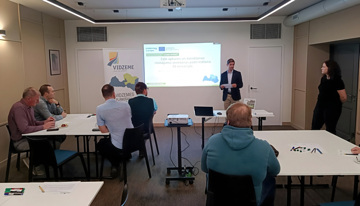 Vīrietis sniedz prezentāciju pie galdiem sēdošiem speciālistiem