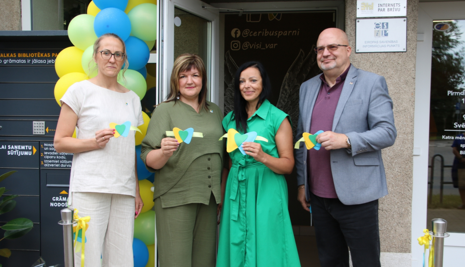 Četri cilvēki tur rokā svinīgas lentes daļas