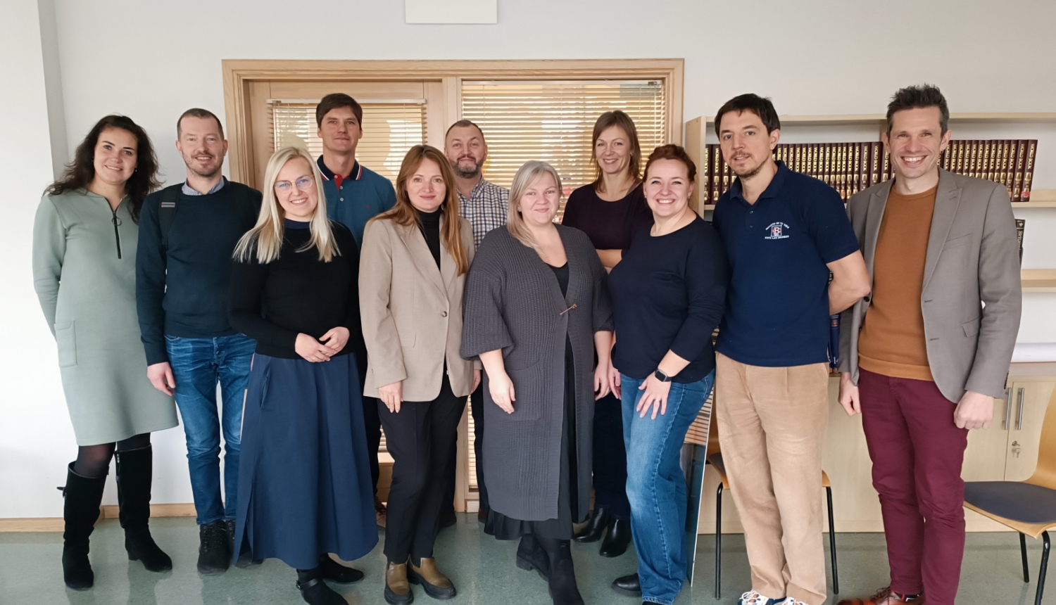 Dažādu profesionāļu grupas kopbilde gaišā, modernā biroja telpā. 