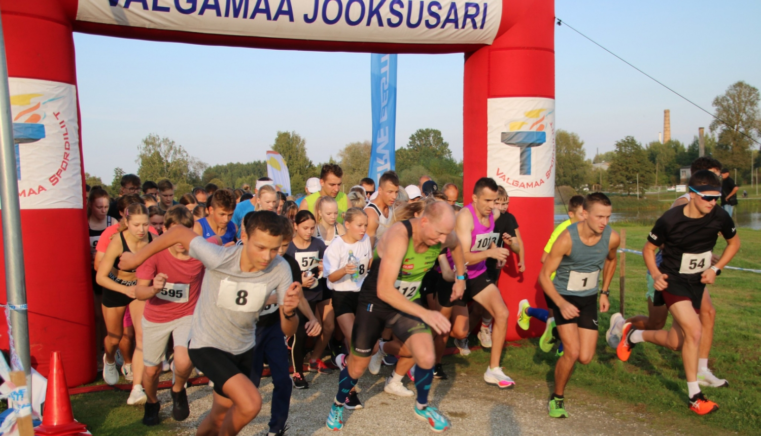 Sacensību dalībnieki skrien pāri starta līnijai