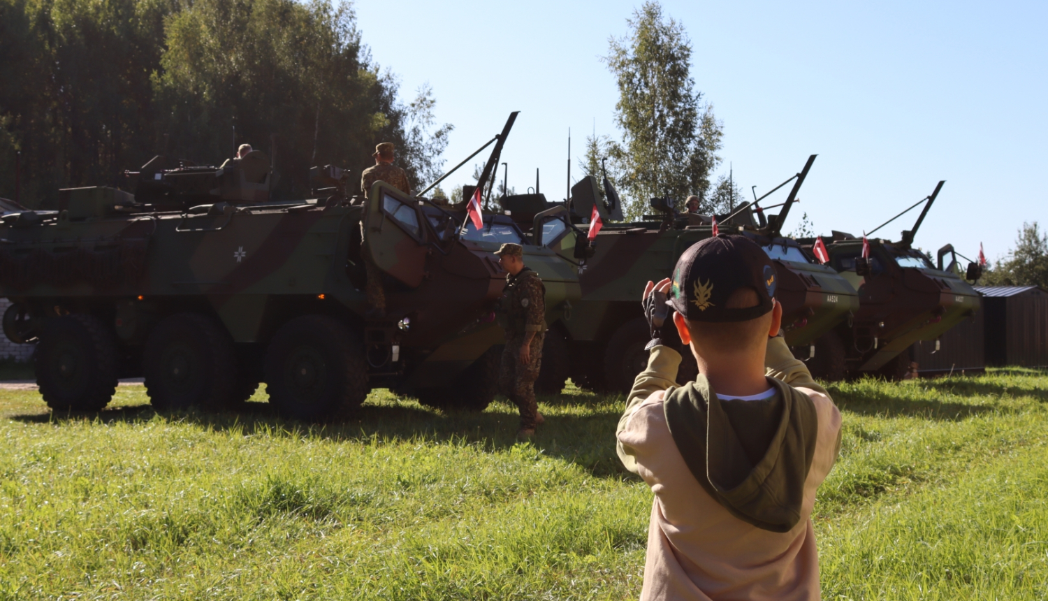 Zēns ar telefonu fotogrāfē rindā sastājušos bruņu transportierus