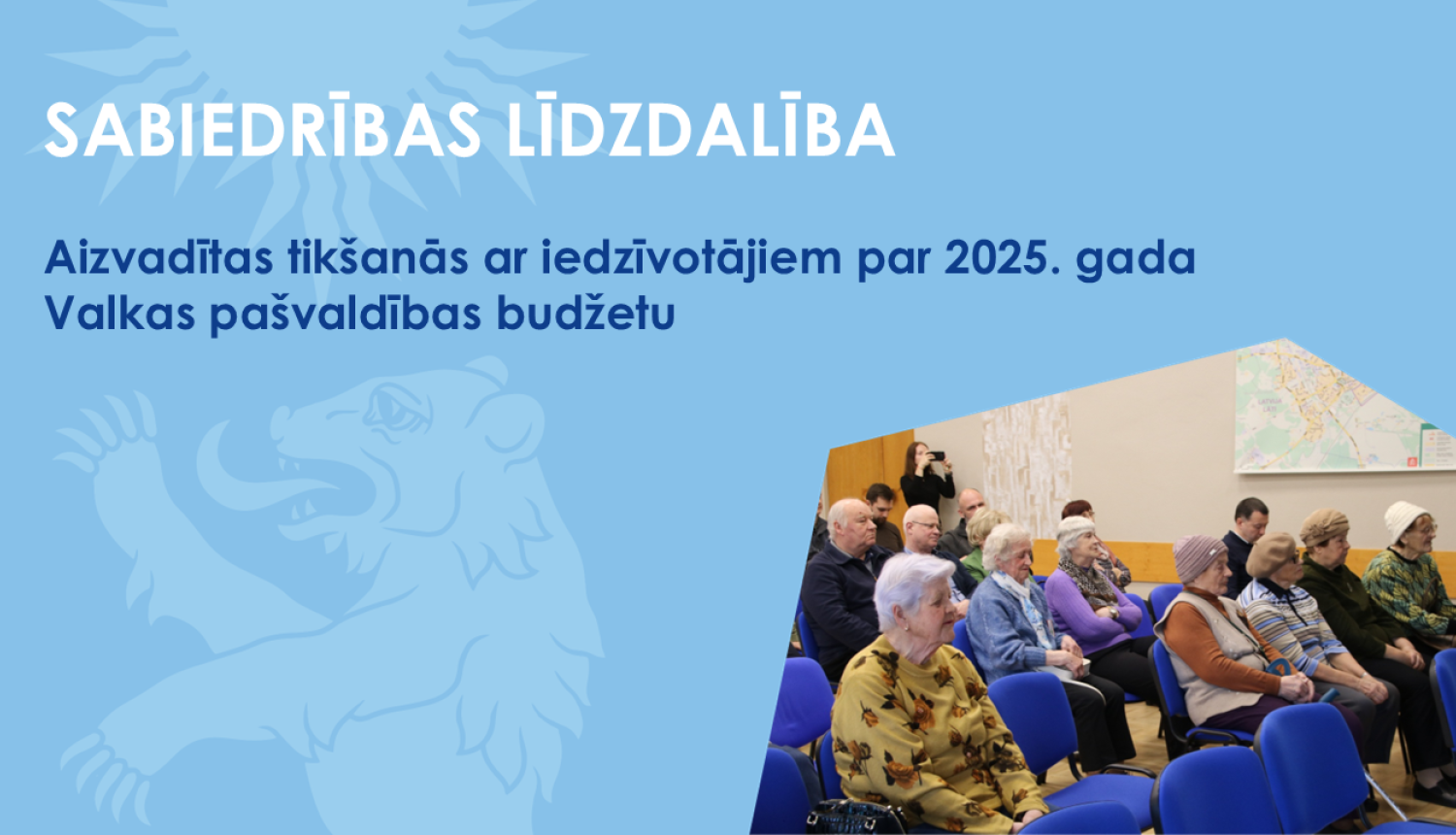 Zils baneris ar Valkas novada pašvaldības lāča ģerboņa siluetu un foto no iedzīvotāju sapulces