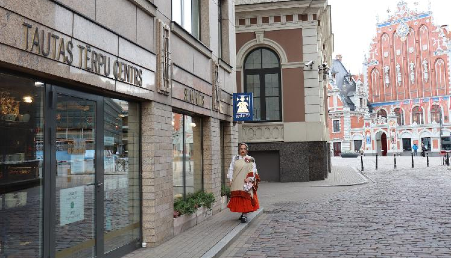 Sieviete latviešu tautas tērpā pie tautas tērpu centra ieejas