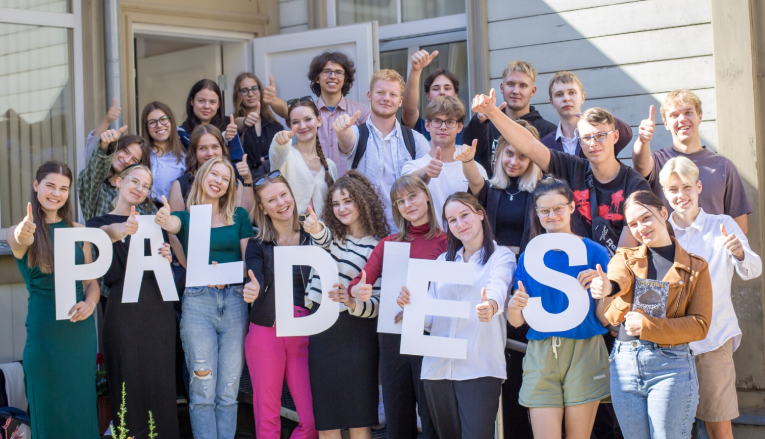 Kopbilde ar Vītolu fonda stipendijas saņēmējiem, kas tur rokās burtus, kas veido vārdu "Paldies"