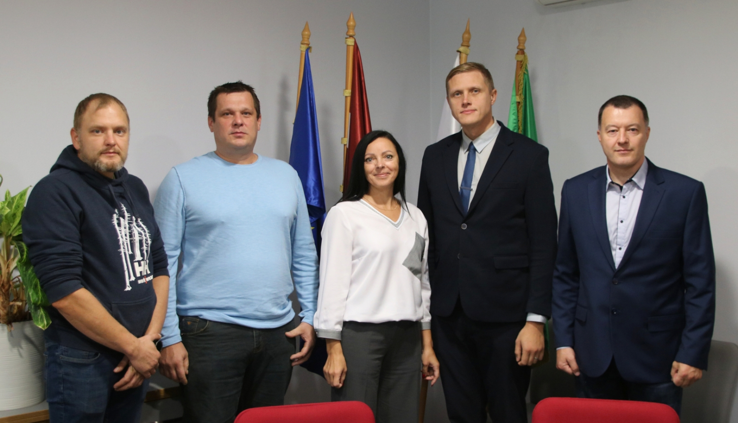 5 cilvēki pie karogiem apspriežu zālē