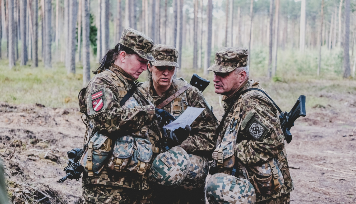 Trīs zemessargi formasterpos meža vidū pēta karti