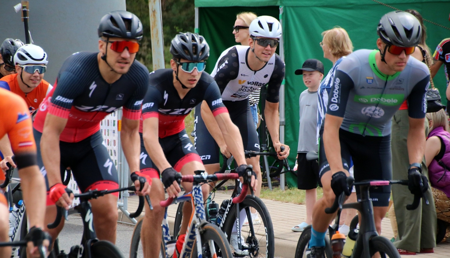 Velobraucēji sportisti krāsainos krekliņos uz riteņiem