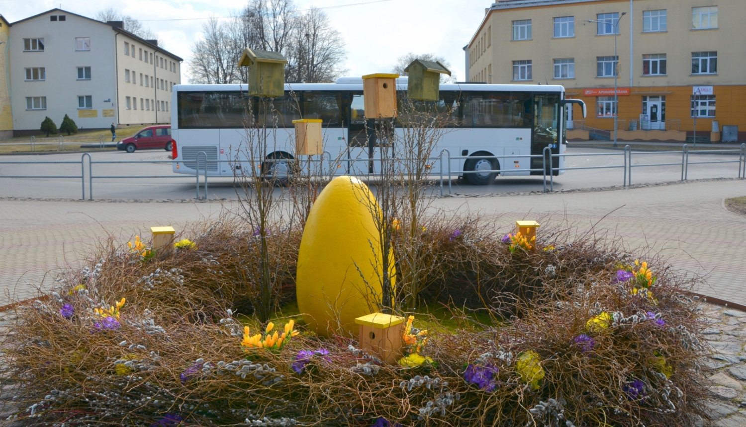 Lieldienu dekorācija - ola grozā priekšplānā un autobuss fonā