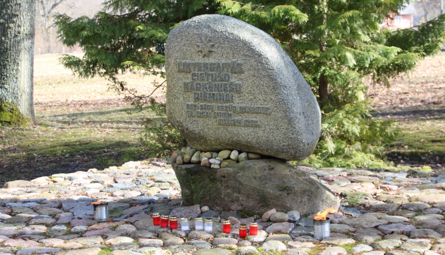 Piemiņas akmens Kārķos, kam apkārt saliktas sarkanbaltsarkanas piemiņas svecītes.