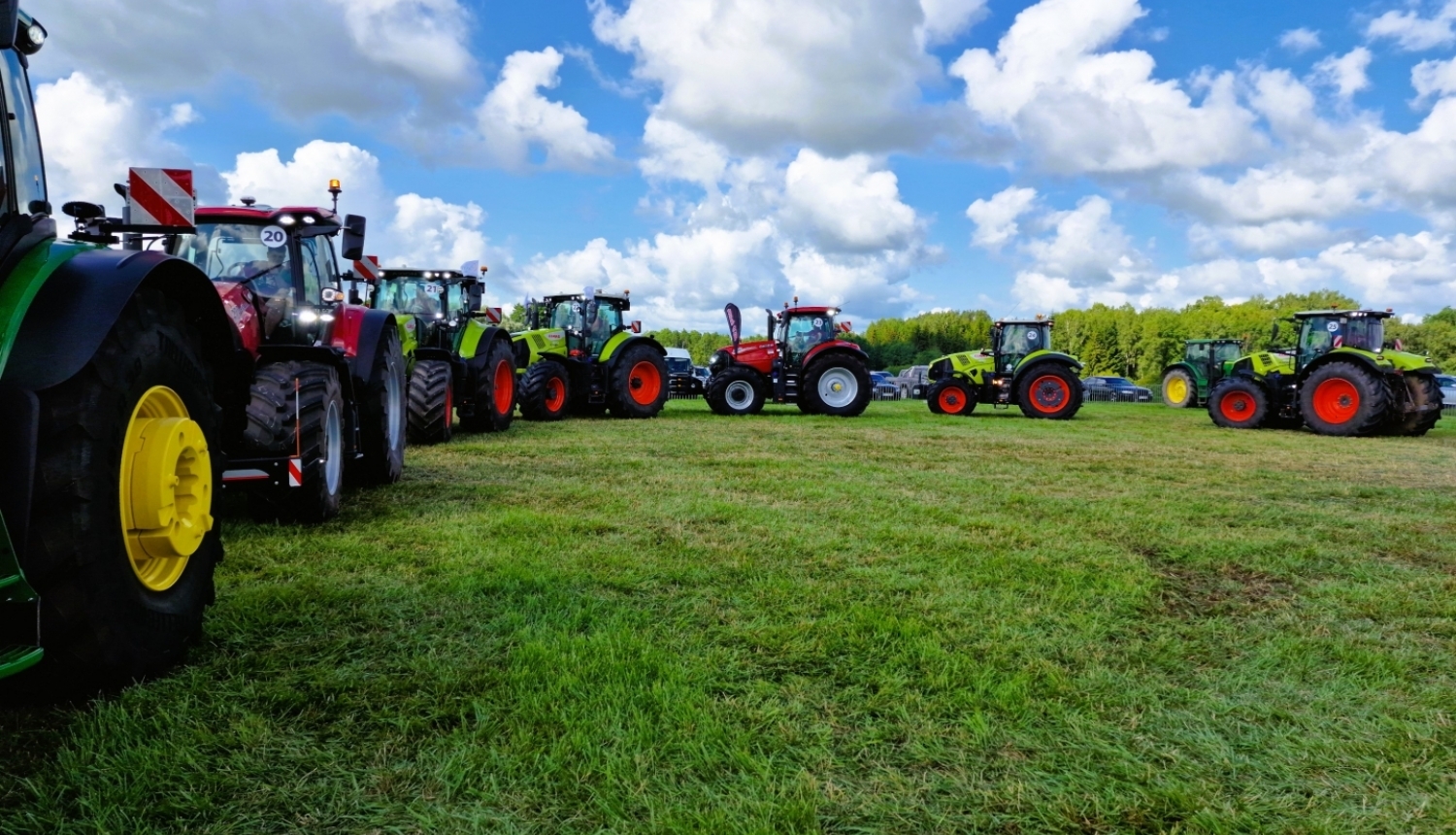 Septiņi dažādas krāsas traktori zaļā pļavā